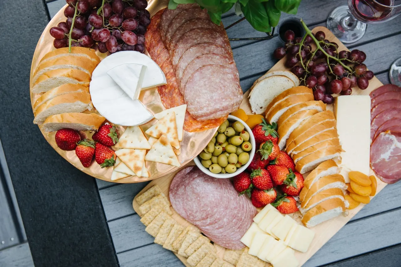 A table with cheese, meats and fruits on it.