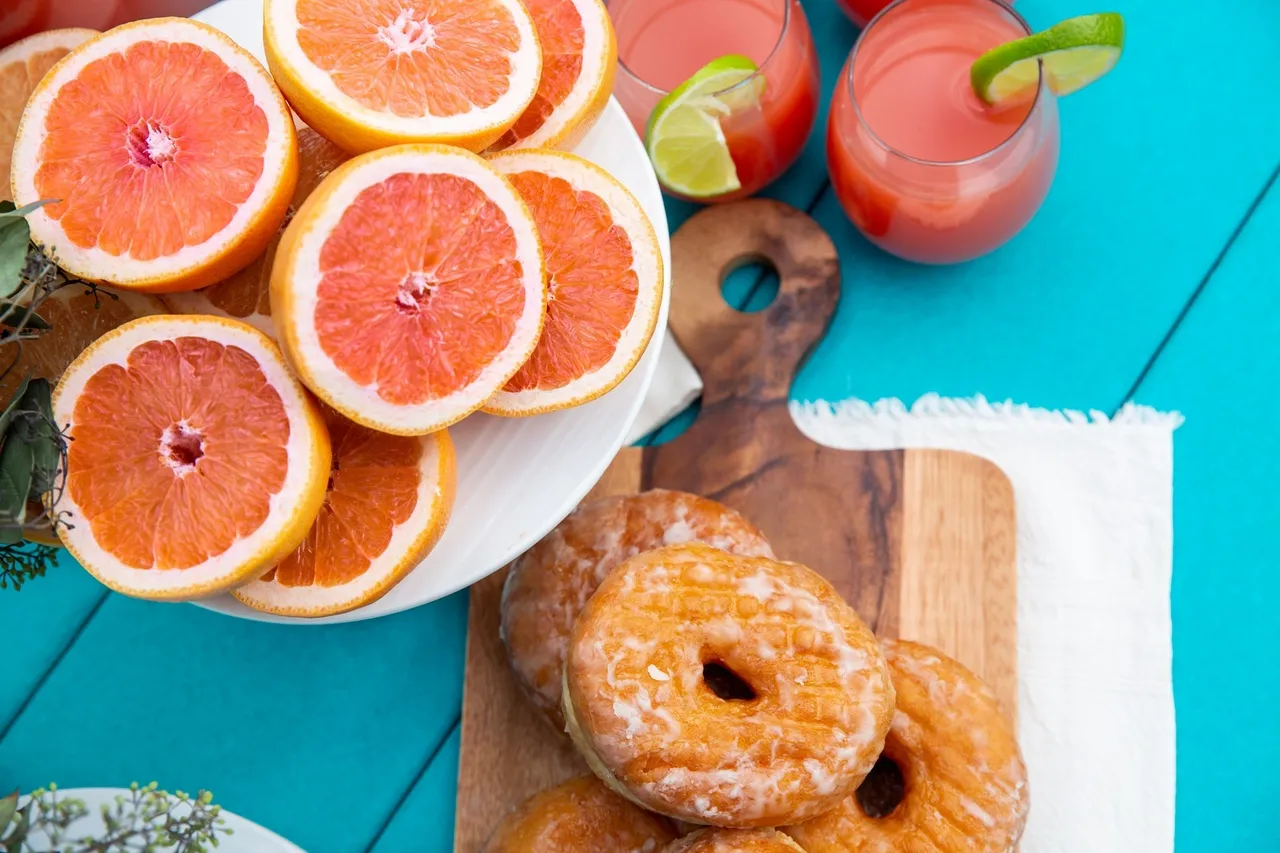 A table topped with grapefruit and donuts next to two glasses.