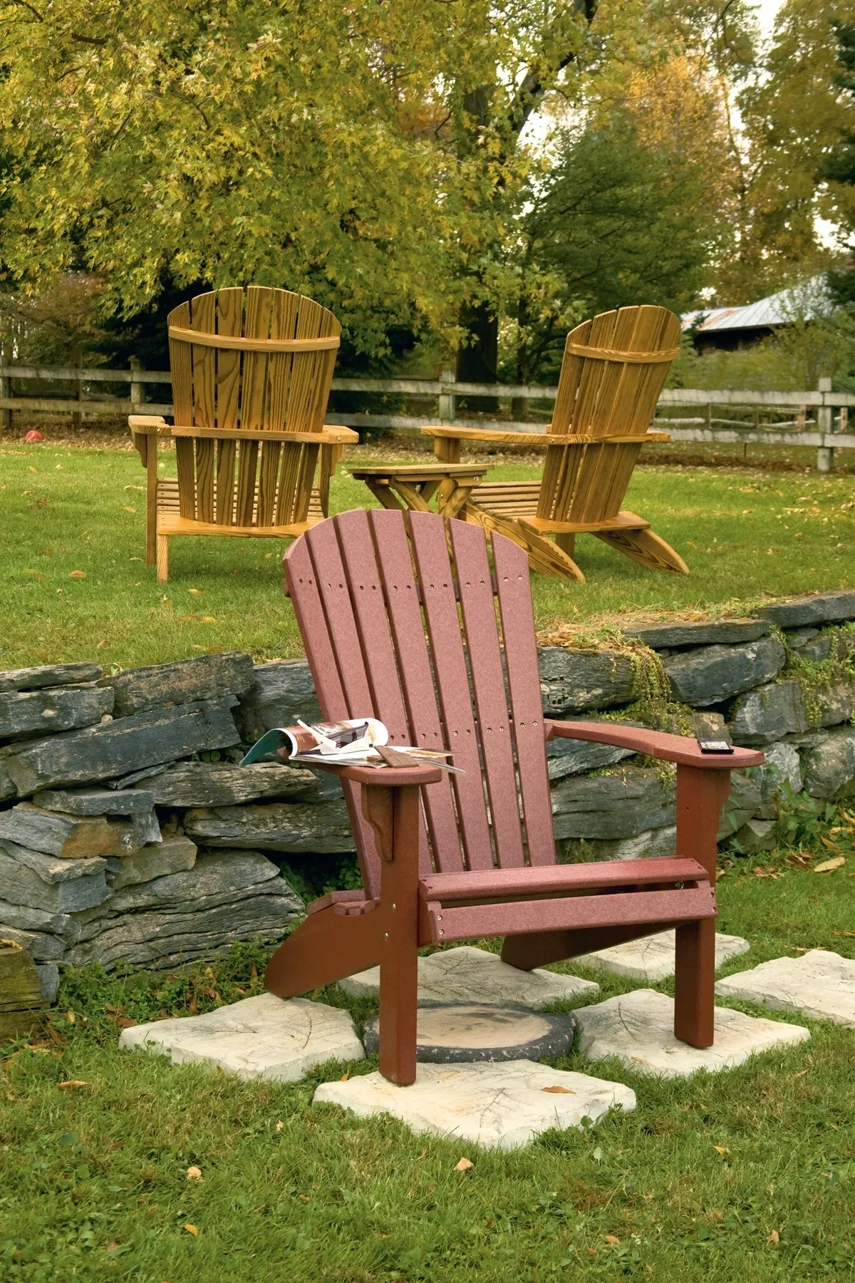 A red chair sitting in the grass next to two wooden chairs.