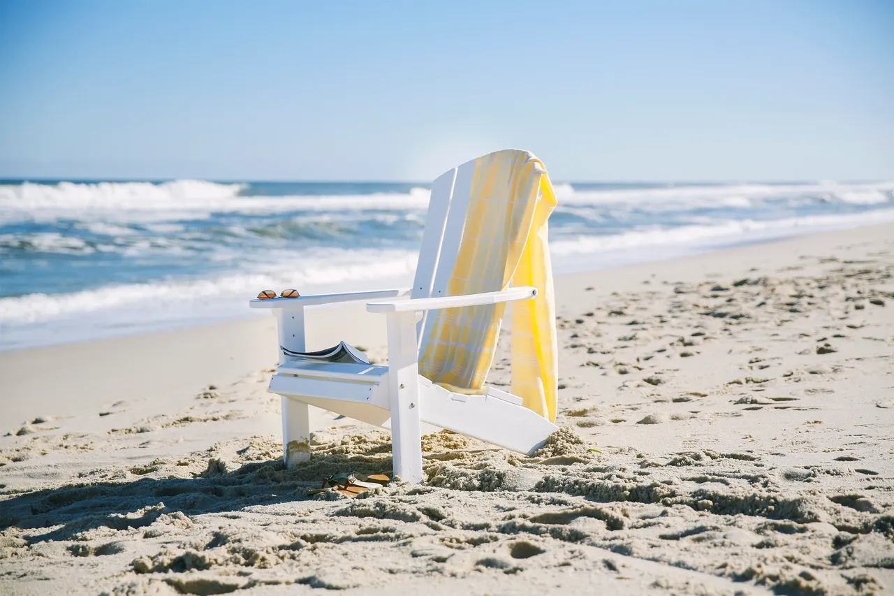 A beach chair with an umbrella on the sand.