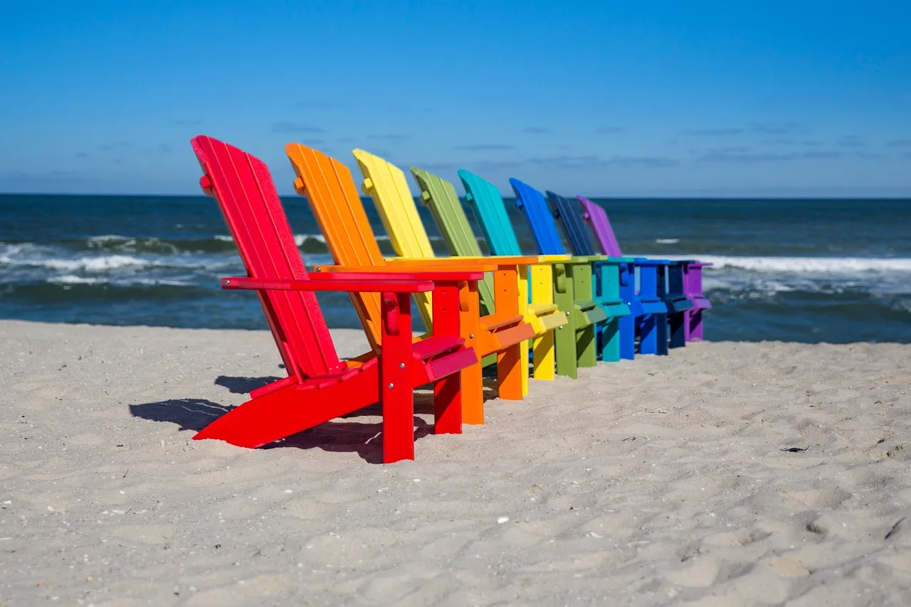 A row of colorful beach chairs on the sand.
