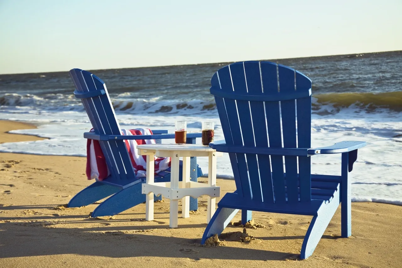 Two blue chairs on the beach with a drink table.