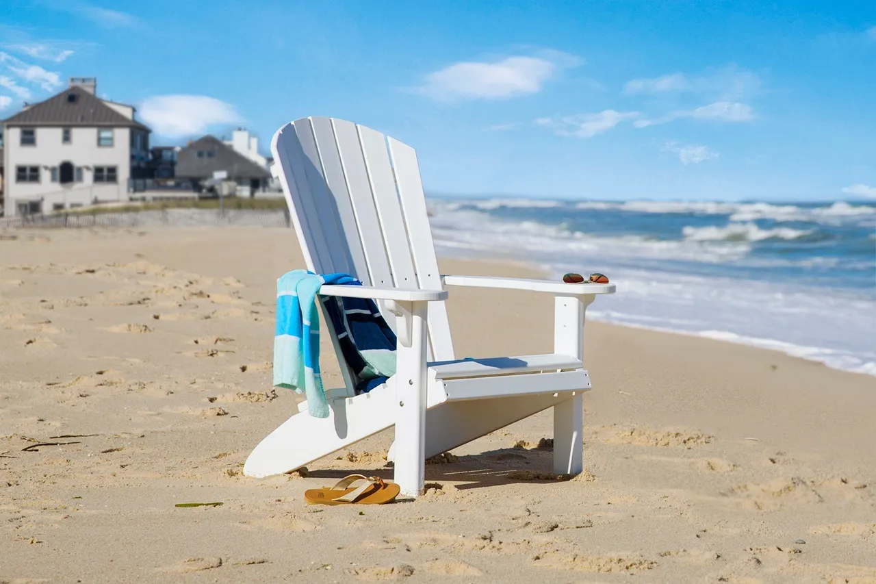 A white chair on the beach with towels hanging from it.