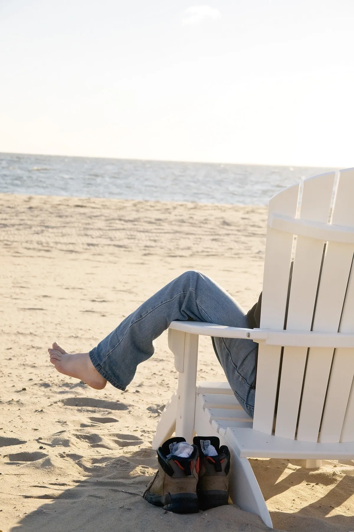 A person sitting on top of an adirondack chair at the beach.
