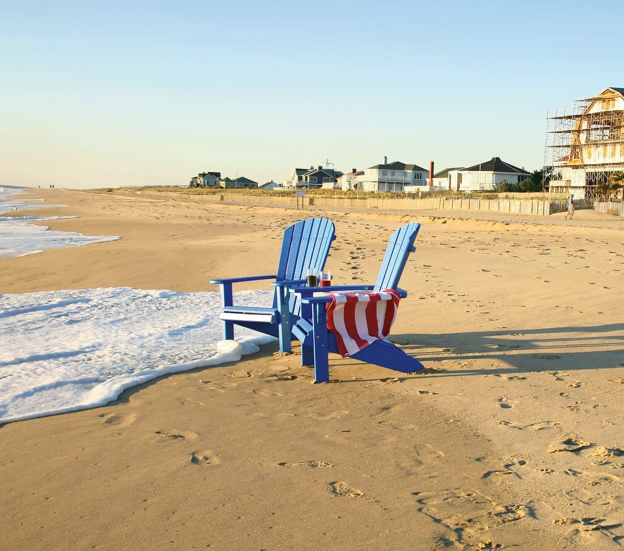 Two lawn chairs on the beach with an american flag chair.